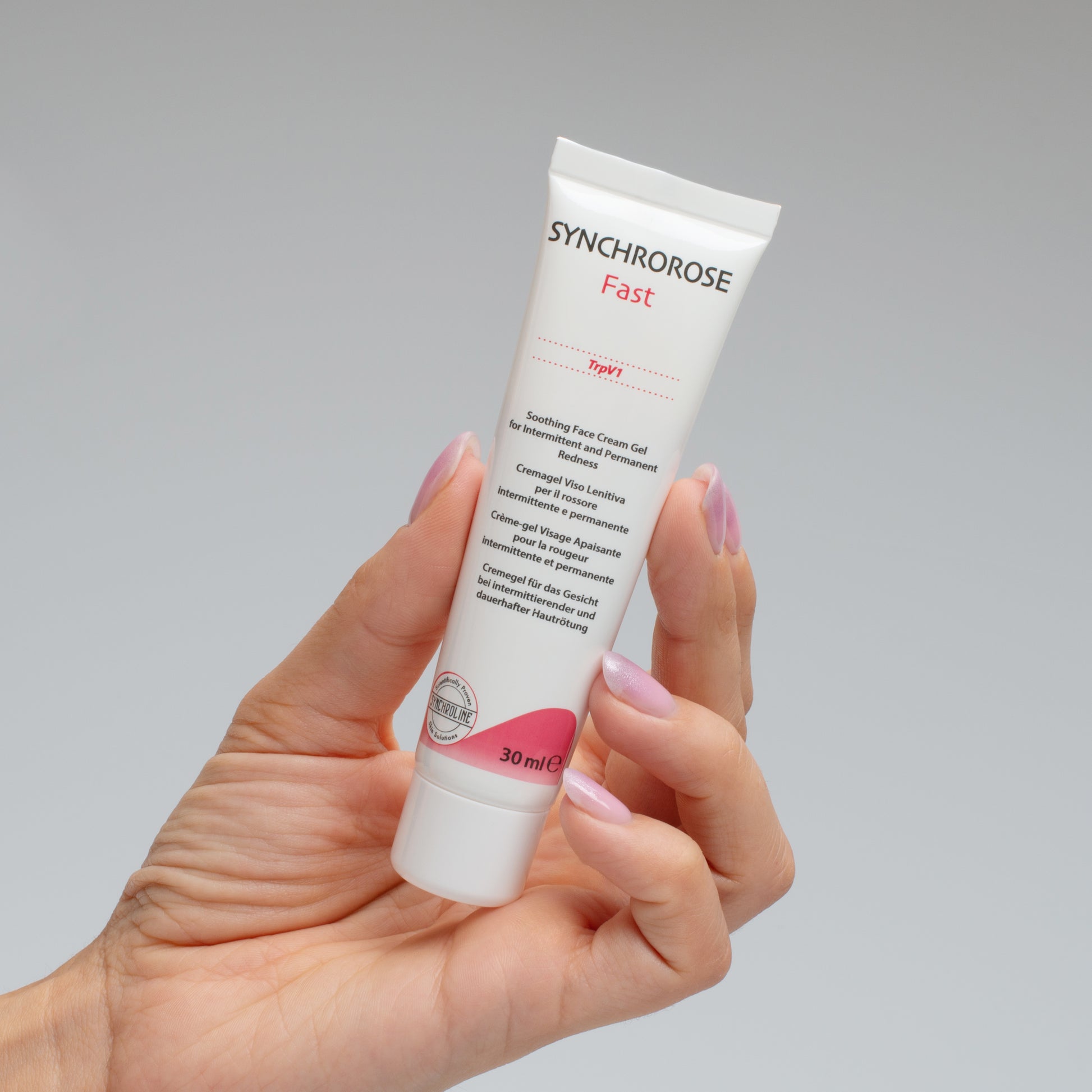 Hand holding a SynchroRose Fast skincare Reactive skin flushing tube against a gray background